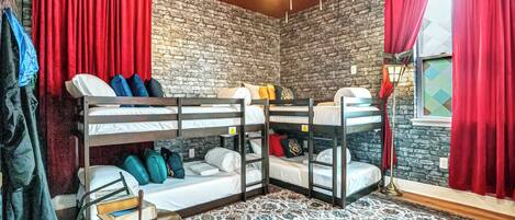 A room with bunk beds, a patterned rug, a round table with books, and a brick wall.