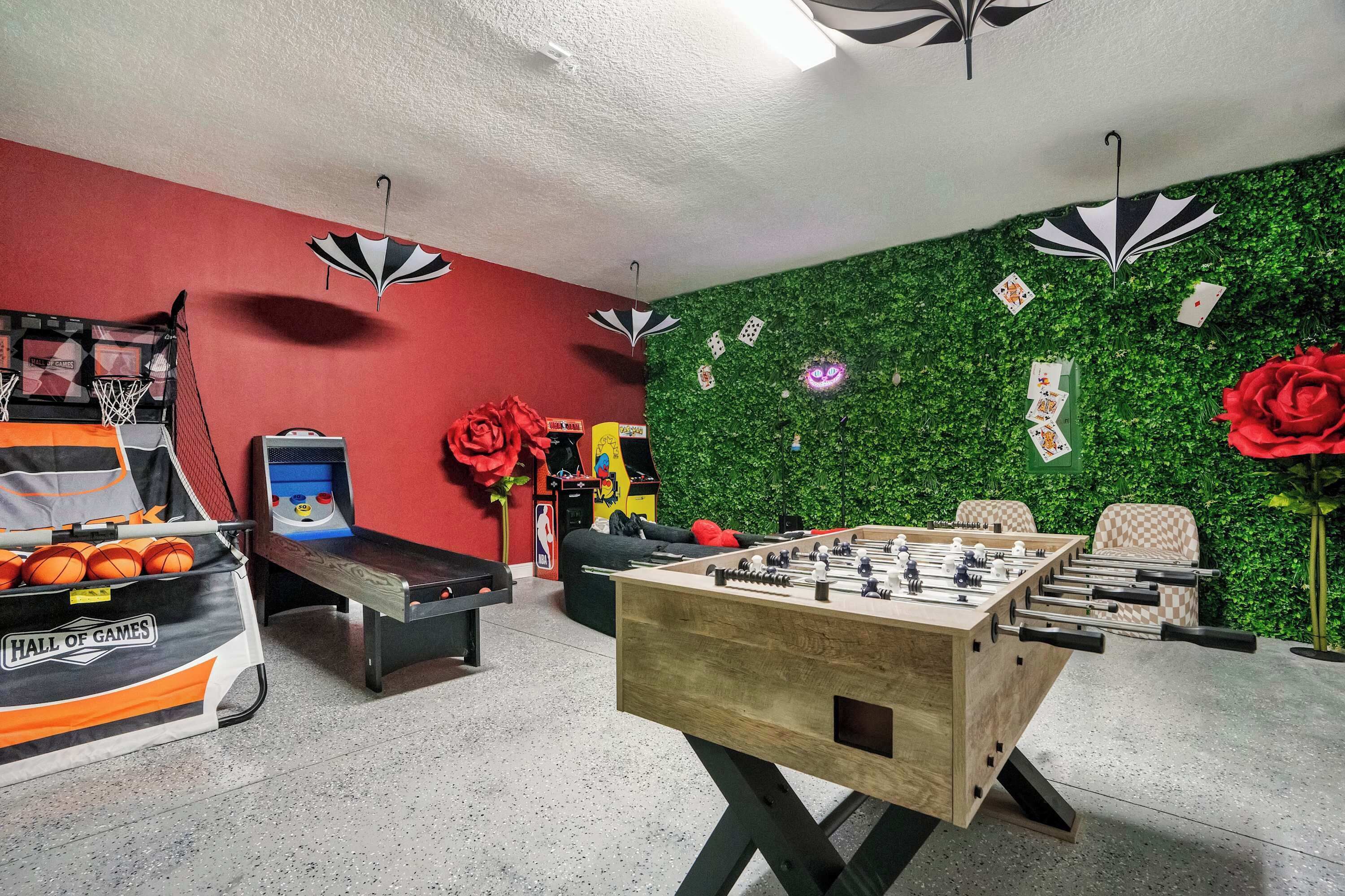 Una habitación con mesa de fútbol de mesa, simulador de baloncesto y pared verde decorada con cartas.