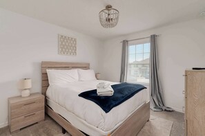 A neatly made bed with a blue blanket, a bedside lamp, and a decorative wall piece. - Family retreat w/ theater, pool & hot tub (Kissimmee)