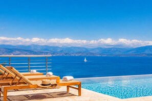 Ein Poolbereich mit Liegestühlen, Handtüchern und Blick auf Meer und Berge.