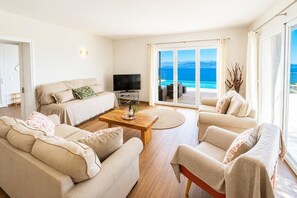 Ein modernes Hotelzimmer mit einer Couch, einem Couchtisch, einem Fernseher und einem Balkon mit Meerblick.