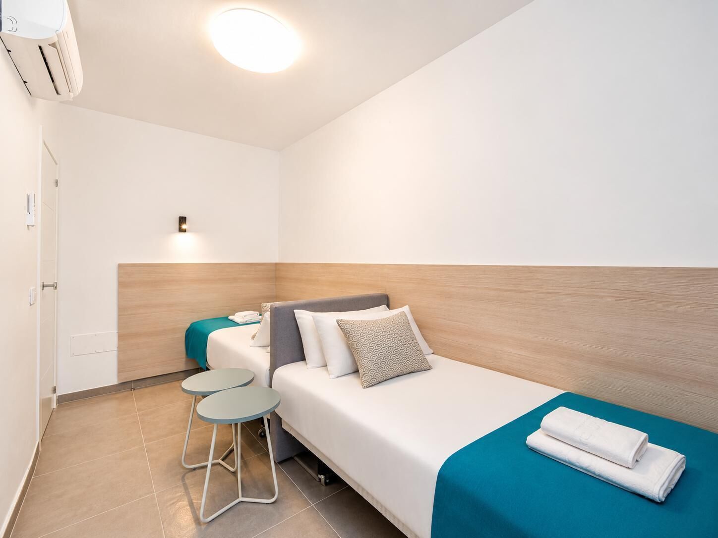 Une chambre d’hôtel avec un lit, une petite table, une chaise et un luminaire au plafond.