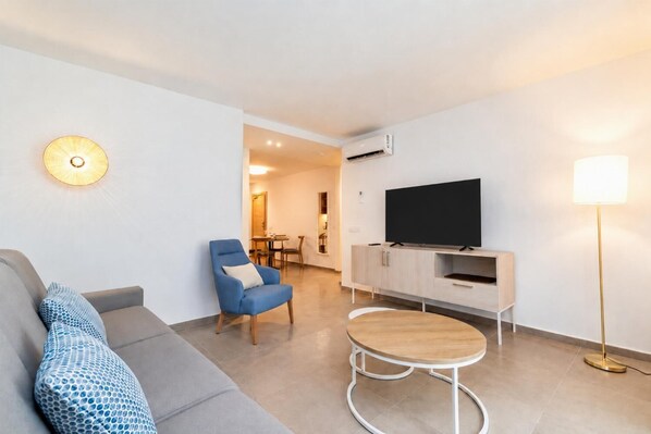 A modern living room with a sofa, a blue armchair, a TV on a wooden cabinet, a small round table, and a floor lamp. - Ereza Residence 1.2 - Two Bedroom Apartment, Sleeps 4 (Arrecife)