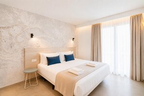 A modern hotel room with a large bed, a small side table, and a view of the outdoors through large windows. - Ereza Residence 1.2 - Two Bedroom Apartment, Sleeps 4 (Arrecife)