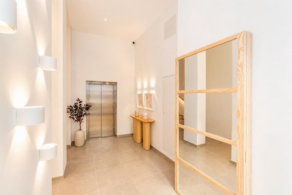 A modern hallway with a wooden-framed mirror, a reception desk with a vase of dried plants, and a wall-mounted light fixture. - Ereza Residence 1.4 - Two Bedroom Apartment, Sleeps 4 (Arrecife)