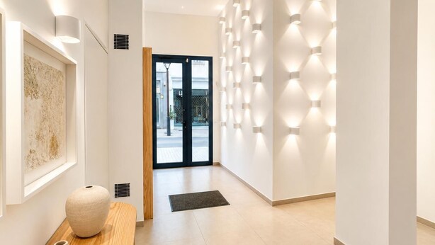 Un pasillo moderno con un banco de madera, un jarrón grande e iluminación en la pared.