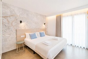 A modern hotel room with a marble wall, a large bed with white bedding, a small stool, and a large window with curtains. - Ereza Residence 5 - Two Bedroom Apartment, Sleeps 4 (Arrecife)