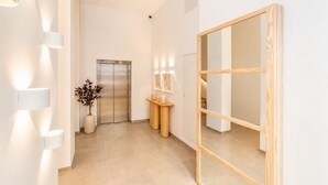 Un pasillo moderno con un espejo de marco de madera, un mostrador de recepción con un florero de plantas secas y un accesorio de luz fijado a la pared.