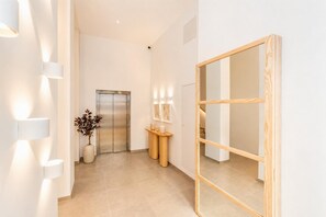 Ein moderner Flur mit einem spiegelnden Wandbild aus Holz, einem Empfangstisch mit einer Vase getrockneter Pflanzen und einer Wandleuchte.