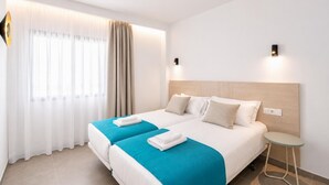 Habitación de hotel con dos camas, una mesita y un ventanal con cortinas.