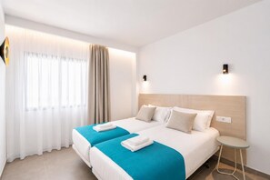 Ein Hotelzimmer mit zwei Betten, einem kleinen Tisch und einem Fenster mit Vorhängen.