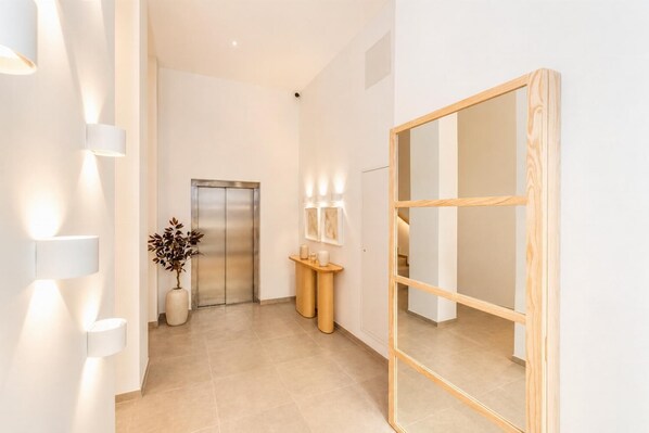 A modern hallway with a wooden-framed mirror, a reception desk with a vase of dried plants, and a wall-mounted light fixture. - Ereza Residence 2.2 - Two Bedroom Apartment, Sleeps 4 (Arrecife)