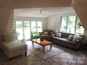 A living room with a sofa, armchair, and coffee table, large windows with a view of greenery, and a ceiling fan. - Geodesic Dome +8 private acre Streamlined-Woodland Homestead + Camping Retreat (Raleigh)