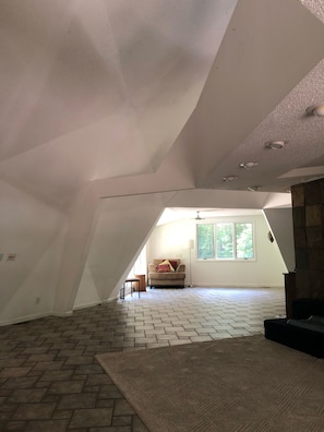 Ein geräumiges Dachzimmer mit einem Fischgrätparkett, einer Couch und einem Fenster.