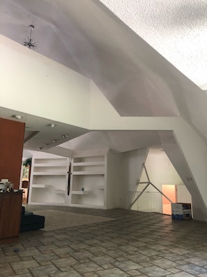 Ein Innenraum mit hohen Decken, freiliegenden Balken und einer Treppe, die in eine untere Ebene führt.