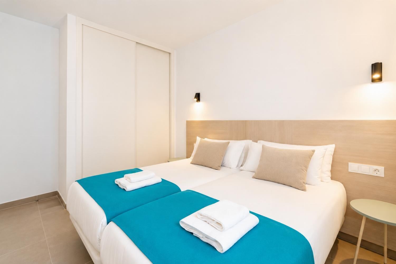 Una camera d'albergo con un letto, due cuscini, un comodino, una lampada a muro e una porta.