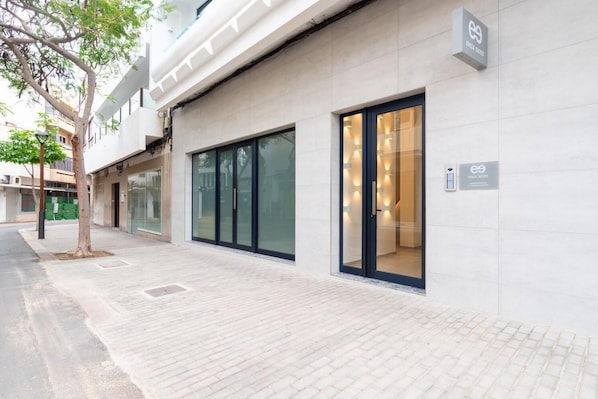 Un edificio moderno con porte e finestre in vetro, un marciapiede pavimentato e un albero.