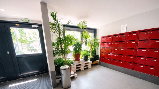 Un vestíbulo limpio y moderno, con una puerta negra, taquillas rojas y plantas en macetas.