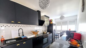Cocina moderna con armarios negros, salpicadero blanco de azulejos y encimera negra.  Hay un comedor con una silla roja y una mesa.