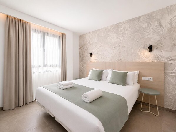 Et moderne hotelværelse med en stor seng, et lille natbord og en lampe monteret på væggen.