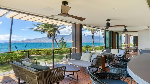 Un espace de détente extérieur moderne, avec des meubles en osier, un bar et une vue sur l’océan.