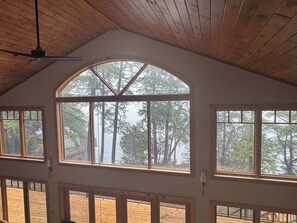 A room with large arched windows, wooden ceiling beams, and a view of trees and a deck outside.