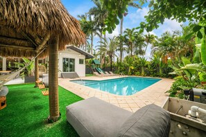Un espace piscine doté d’un toit de chaume, de chaises longues et d’une petite maison.