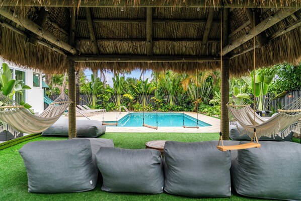 A poolside area with a thatched roof, lounge chairs, and a pool.