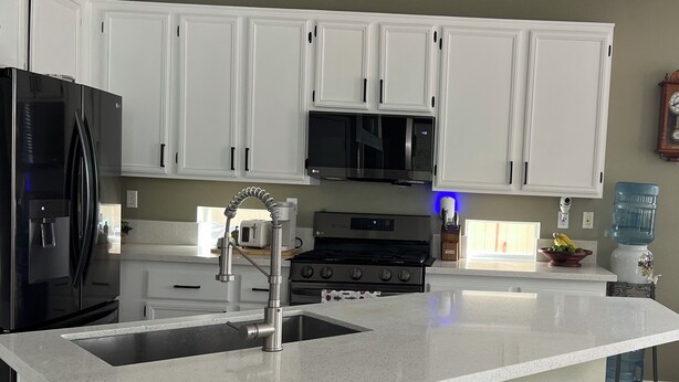 A kitchen with white cabinets, a black refrigerator, a microwave, a stove, a sink, and three wooden stools. - Cozy 1-bedroom house in superb Valley Center with AC (Valley Center)