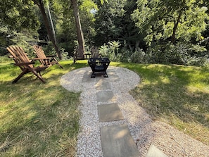 A garden with a gravel path, wooden chairs, and a fire pit.