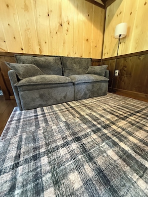 A sofa with a plaid throw blanket, wooden walls, and a floor lamp.