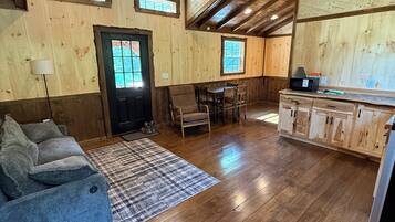 Une pièce spacieuse dotée de planchers en bois, d’un ventilateur de plafond, d’un coin repas avec des chaises, d’un canapé et d’un coin cuisine avec des placards.