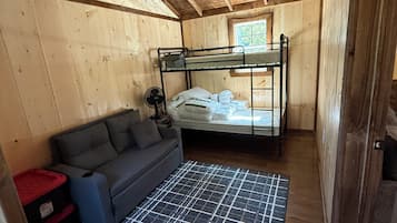L’intérieur d’une cabane en bois, avec des lits superposés, un canapé, un ventilateur et une fenêtre.
