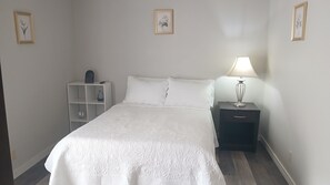 Un dormitorio ordenado con cama, mesitas de noche y velador.