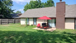 Una casa con patio, una parrilla y un paraguas rojo.
