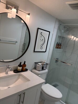 Uma casa de banho moderna com uma pia branca, um espelho grande, uma obra de arte emoldurada e uma cabine de duche em vidro.