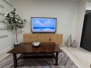 A modern living room with a wooden table, a television on a stand, a potted plant, and decorative vases. - New, Cozy 1-Bed, Bsm Suite. with AC in Beautiful Edmonton, Prívate Entry. (Edmonton)