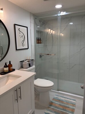 Ein modernes Badezimmer mit Duschkabine aus Glas, einer weißen Toilette und einem Waschbecken mit Pflegeprodukten.