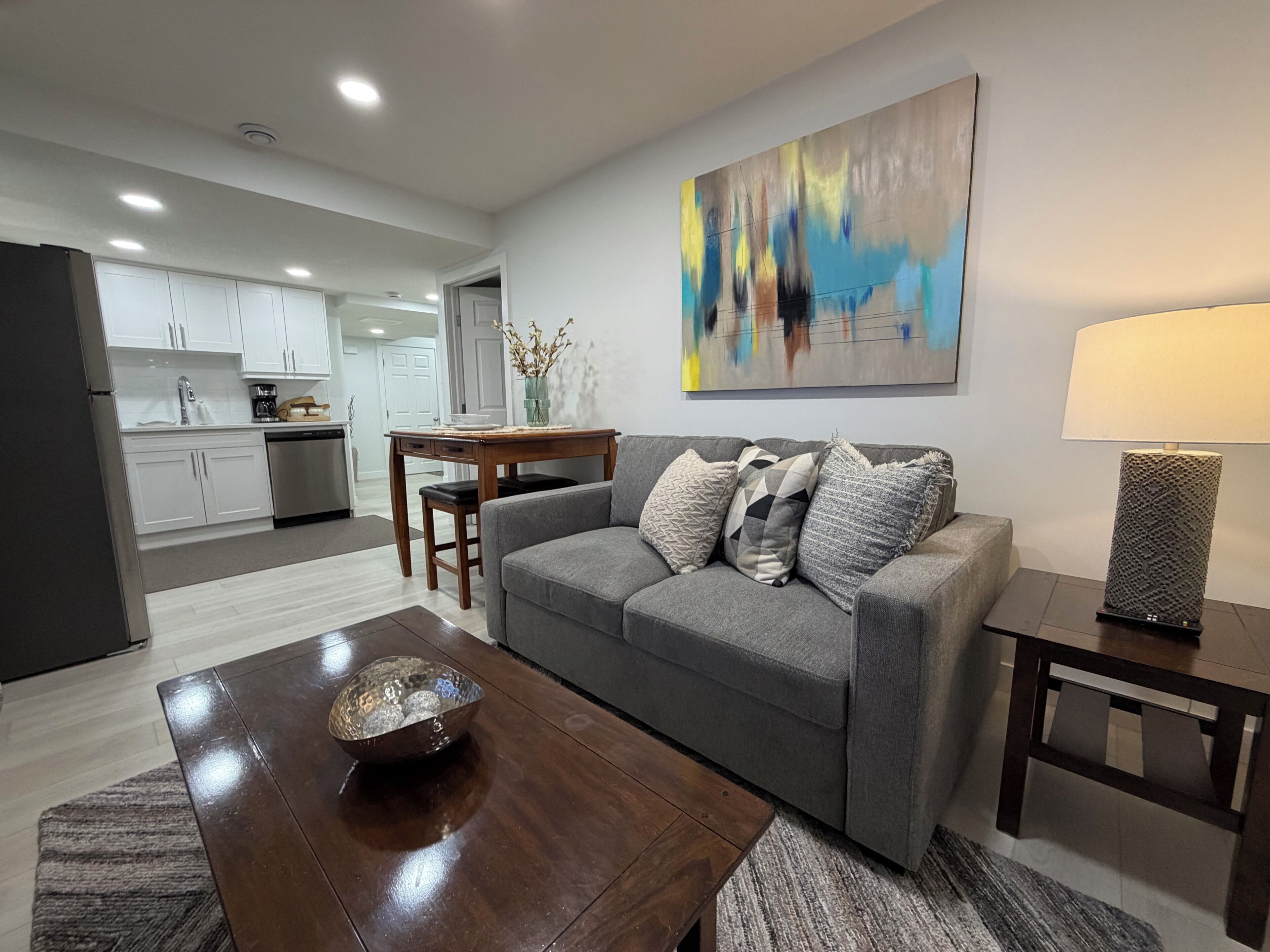 A modern living room with a grey sofa, a wooden coffee table, and a painting on the wall.