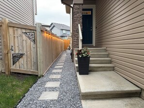 Ein Weg führt zu einem Haus, begleitet von einem Holzzaun, einer Steinpfeiler und einem Blumenbeet an den Stufen.