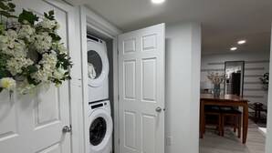 A laundry room with a washing machine, a door with a floral wreath, and a dining area with a table and chairs. - New, Cozy 1-Bed Room, Bsm Suite. with AC in Beautiful Edmonton, Prívate Entry. (Edmonton)