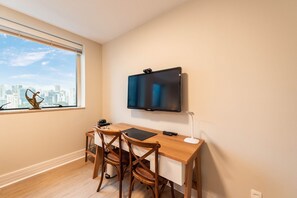 A room with a desk, two wooden chairs, a TV mounted on the wall, and a window with a city view. - Studio on Faria Lima With Pool and Spa - Bt1110 (São Paulo)