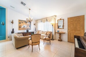 A living room with a sofa, chairs, a dining table, a chandelier, a piano, and a large painting on the wall. - 3BR Vegas Home Jacuzzi Suite • BBQ • Pet Friendly (Las Vegas)