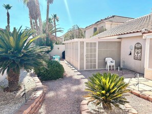 A courtyard with palm trees, a covered patio area, and a white chair. - 3BR Vegas Home Jacuzzi Suite • BBQ • Pet Friendly (Las Vegas)