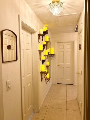 A hallway with white doors, a wall-mounted candle holder, and a chandelier. - 3BR Vegas Home Jacuzzi Suite • BBQ • Pet Friendly (Las Vegas)