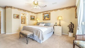 Ein Schlafzimmer mit einem Bett, Nachttischen, einer Bank, einem Deckenventilator und Kunstwerken an den Wänden.
