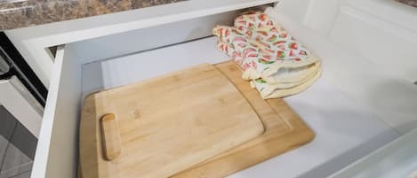 A kitchen drawer with a wooden cutting board and a cloth with a watermelon pattern.