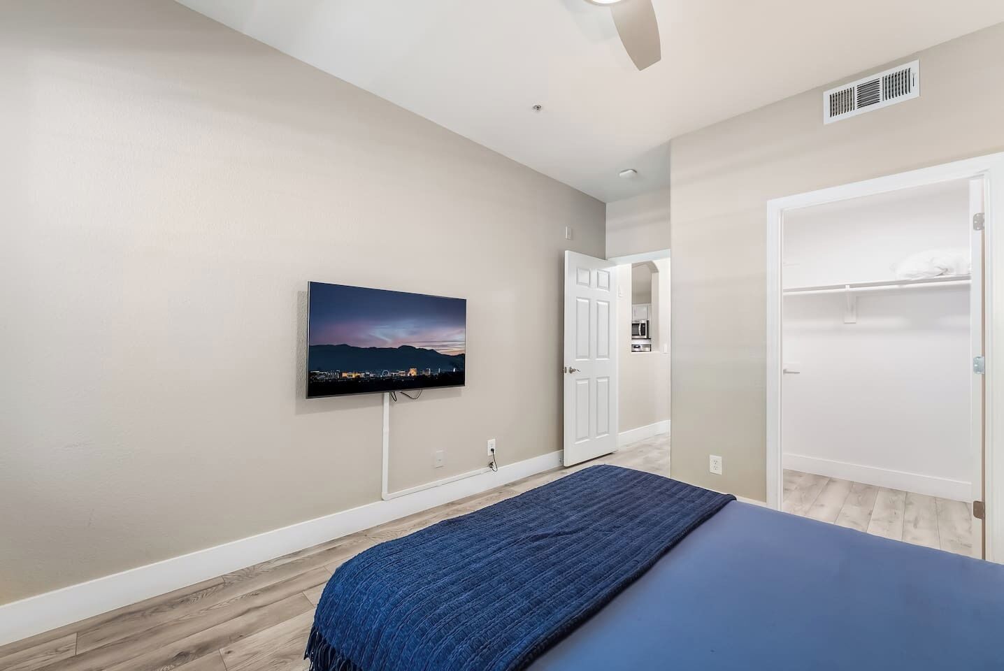 A bedroom with a bed, a television mounted on the wall, a door leading to a bathroom, and a closet.
