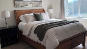 A bedroom with a wooden bed, two bedside tables with lamps, a painting on the wall, and a window with a view.