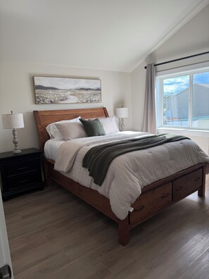 Une chambre Ă coucher avec un lit en bois, deux tables de chevet avec des lampes, un tableau au mur et une fenĂȘtre donnant sur un paysage.